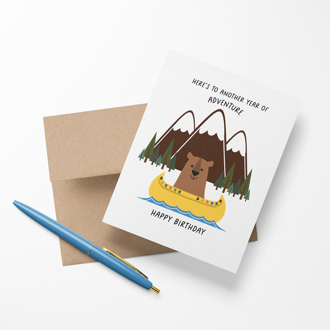 Birthday card with bear in a canoe and mountain background on a Kraft envelope. 