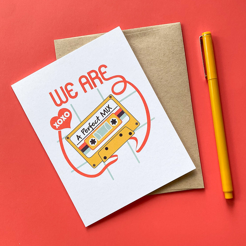 Illustrated greeting card with cassette tape design and 'WE ARE A Perfect Mix' text with a kraft envelope and yellow pen on a red background.