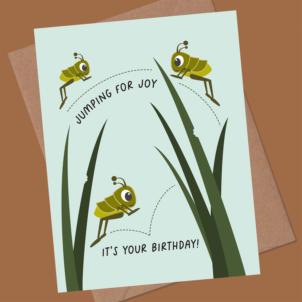 Birthday card with cartoon grasshoppers and text 'Jumping for joy, it's your birthday!' on a brown background