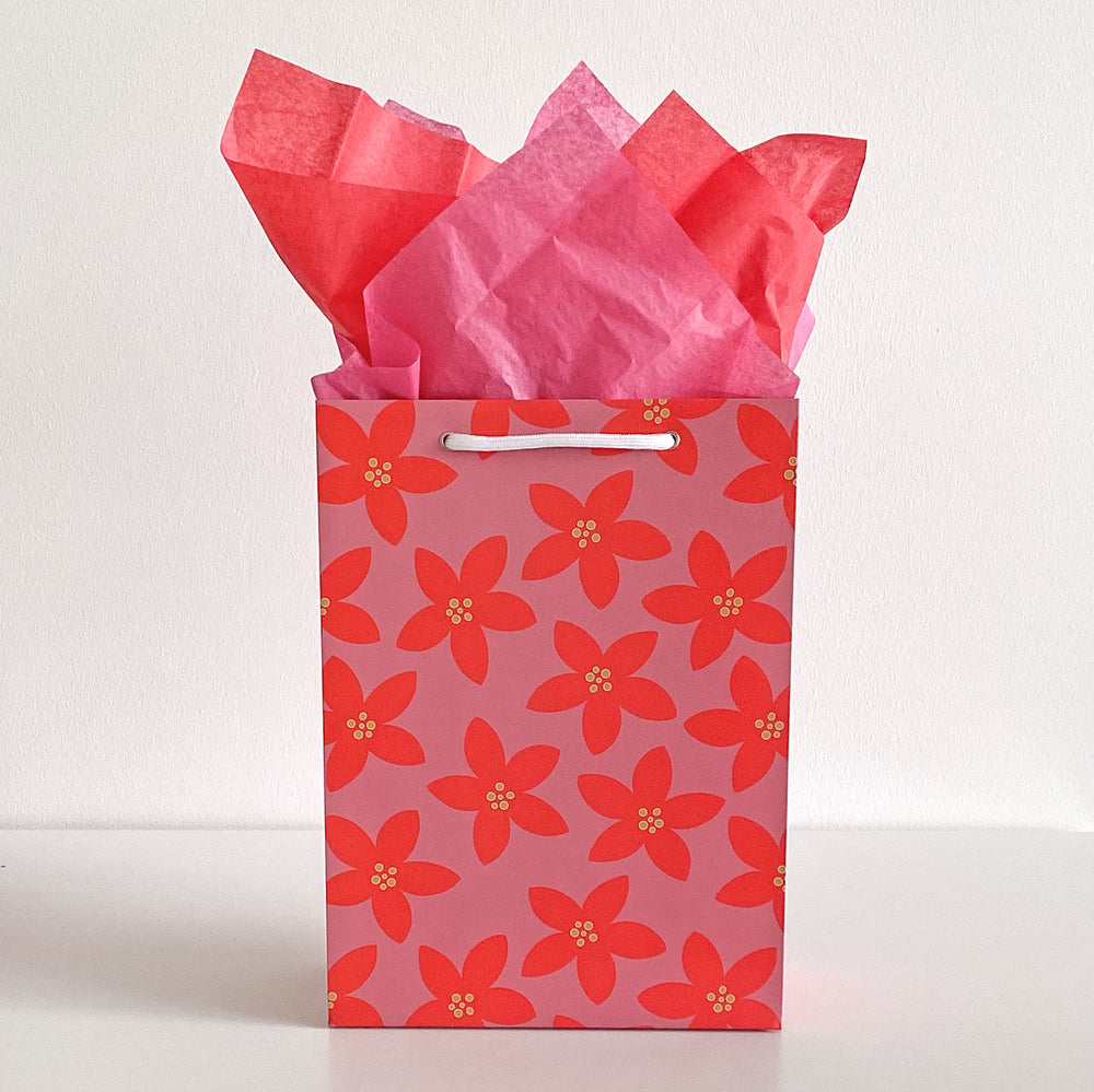 Gift bag with red floral pattern and pink tissue paper on a white background