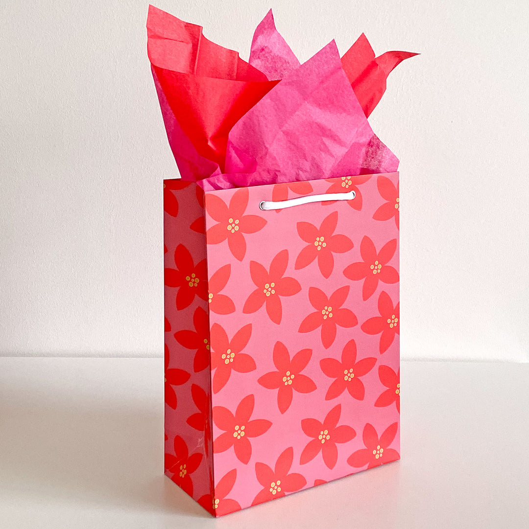 Pink floral gift bag with red tissue paper on a white background