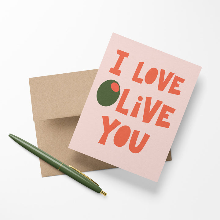 Greeting card with the words, "I love olive you" on a pink background with a Kraft envelope. Shown with a pen.