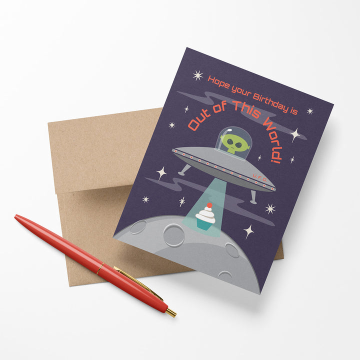 Space-themed birthday card with alien and UFO design on a dark blue background shown with an envelope and pen.