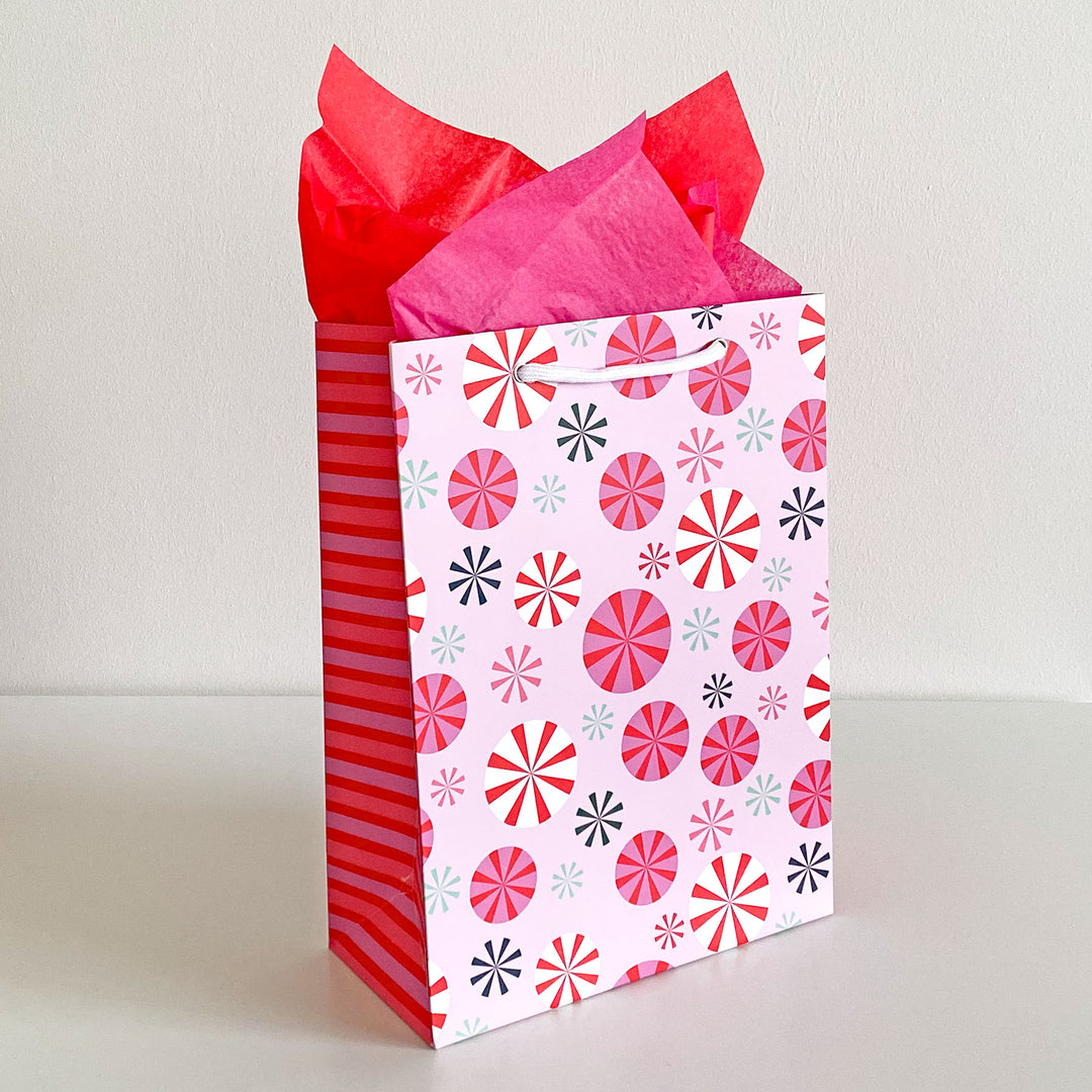 Peppermint patterned gift bag with red and pink tissue paper on a white background