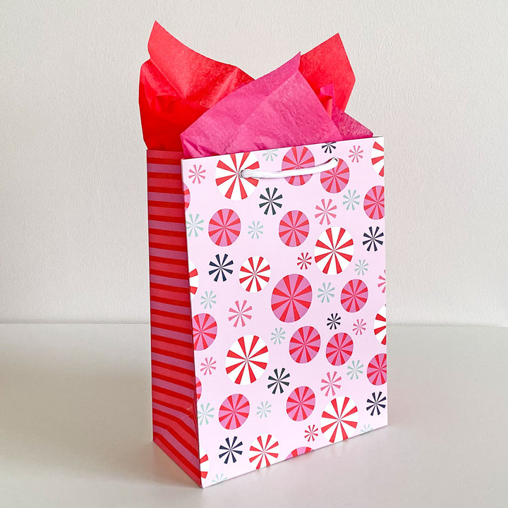Peppermint patterned gift bag with red and pink tissue paper on a white background