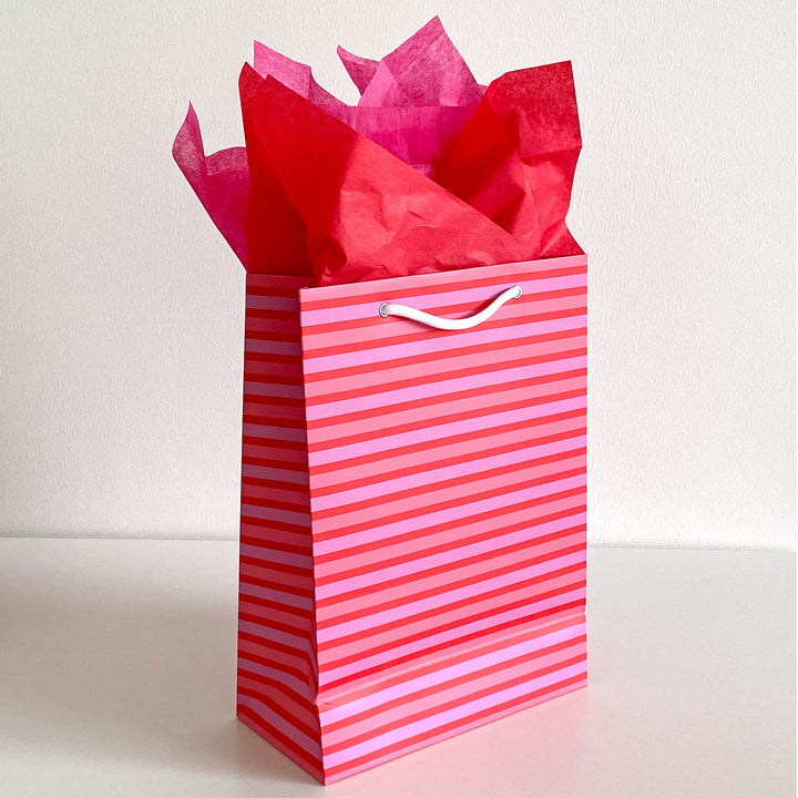 Pink and red striped gift bag with red tissue paper on a white background
