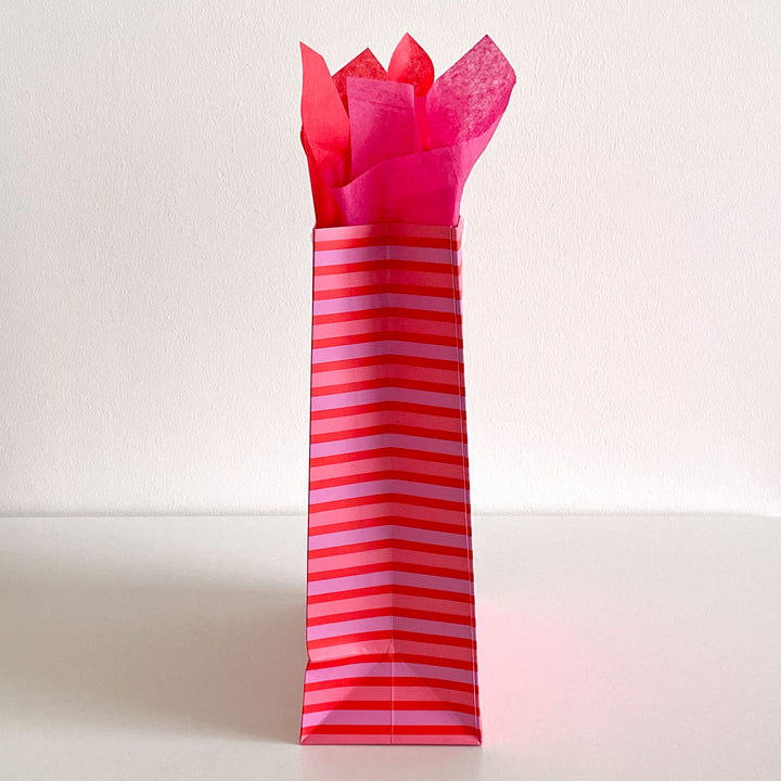 Side view of a pink and red striped gift bag with red tissue paper on a white background