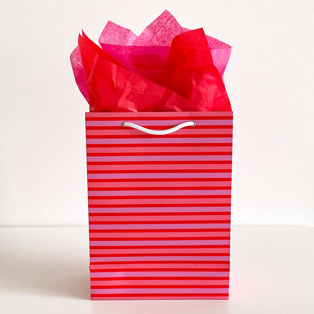 Pink and red striped gift bag with red tissue paper on a white background