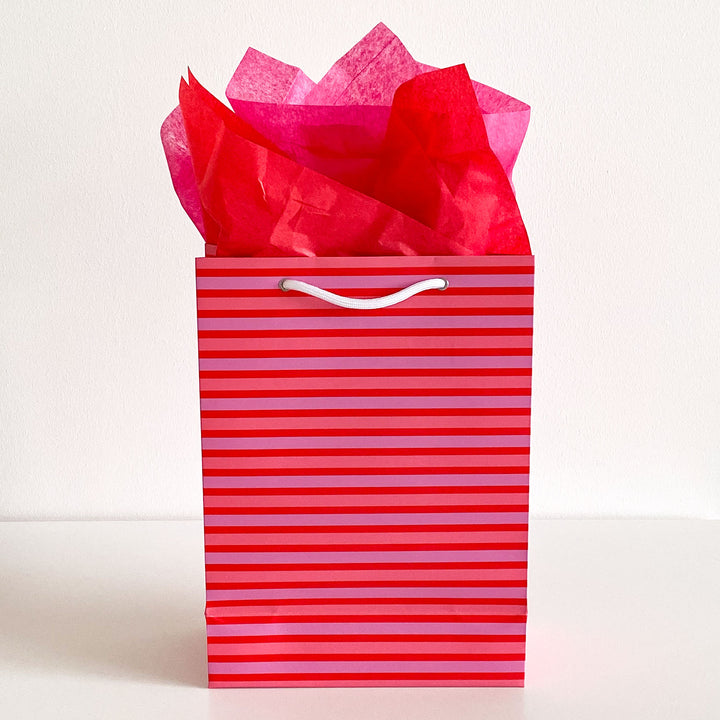 Pink and red striped gift bag with red tissue paper on a white background