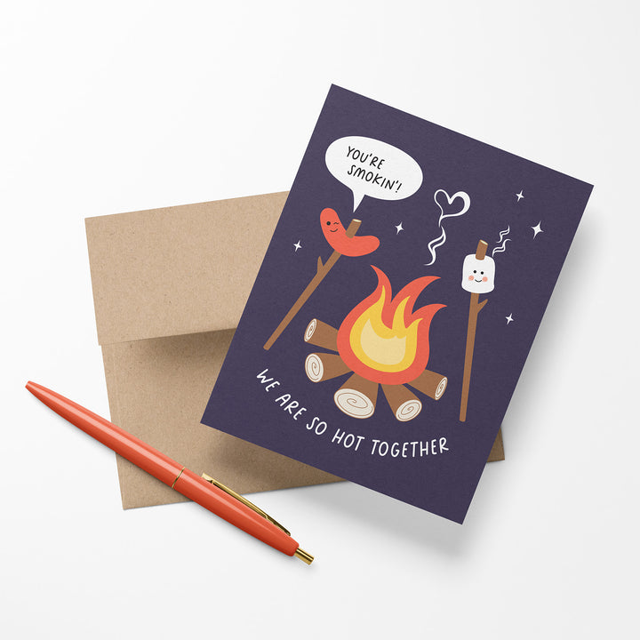 Card with a campfire illustration and romantic text shown with an envelope and pen.