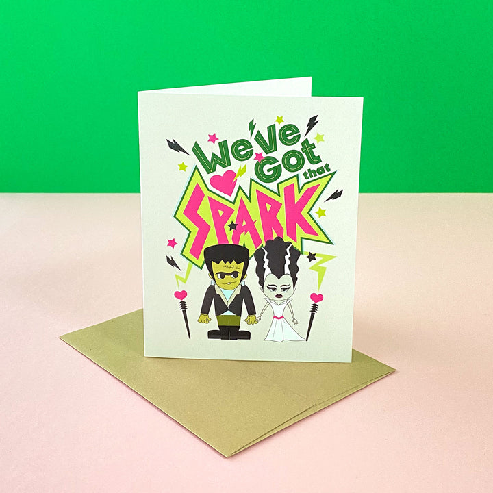 Love greeting card featuring a fun Frankenstein and his bride illustration and hand-lettered saying, "We've got that spark" by Gigglemgg®.