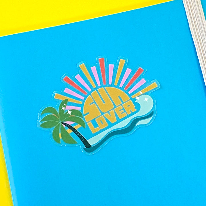 Die-cut vinyl sticker with 'Sun Lover' design on a blue notebook.