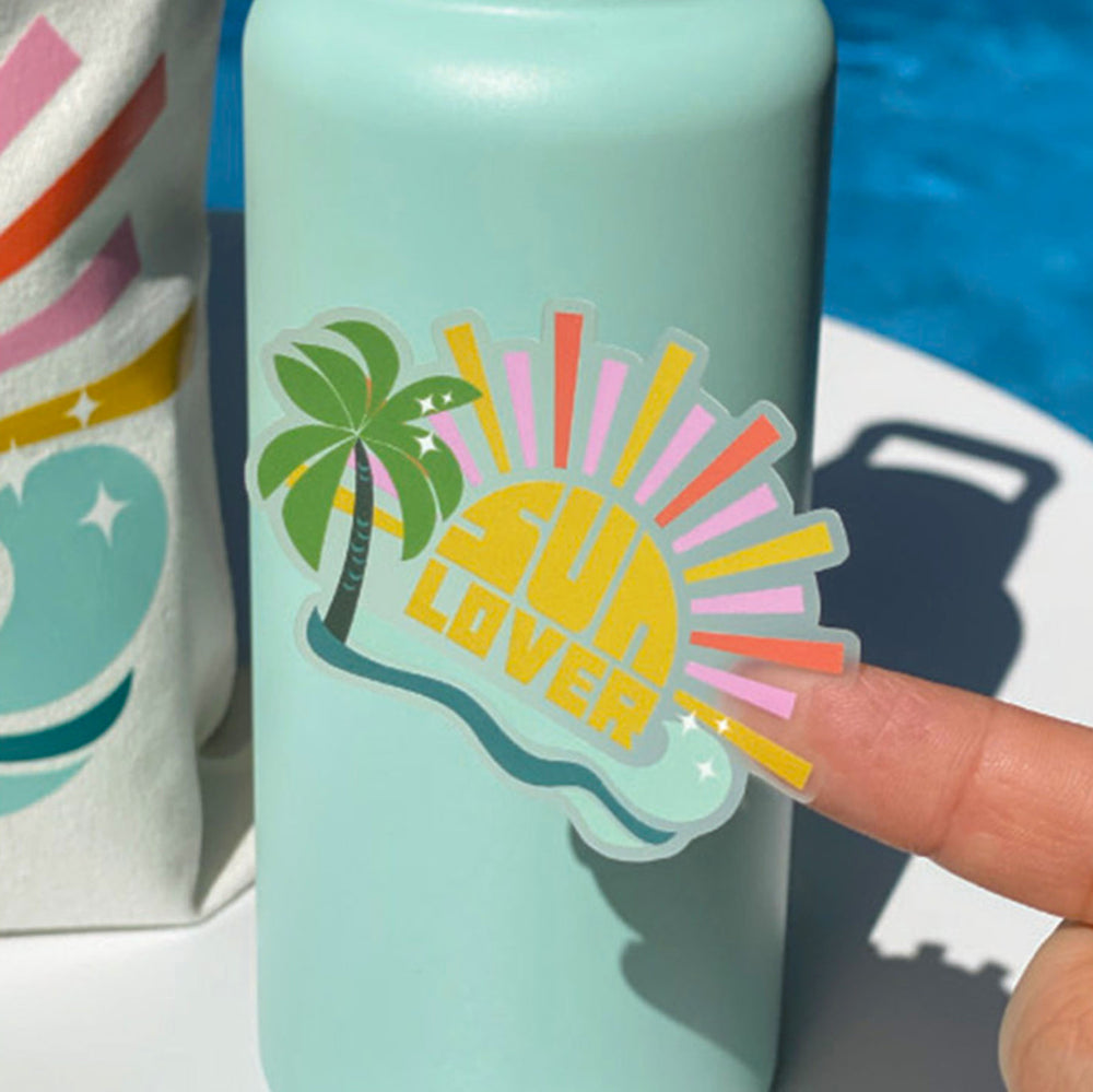 Light blue water bottle with 'Sun Lover' sticker held by a finger, pool visible in background