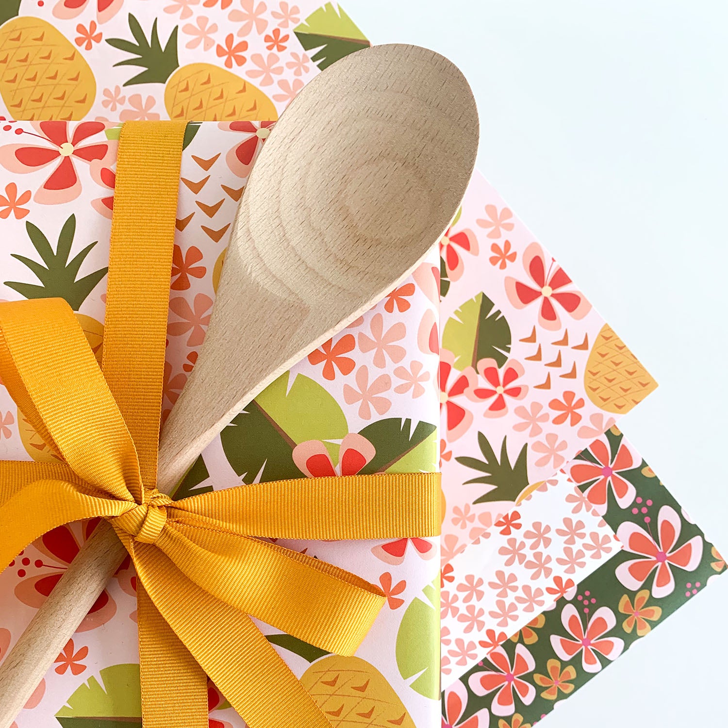 Wooden spoon tied with a yellow ribbon on a colorful floral and pineapple patterned paper by ©Gigglemugg