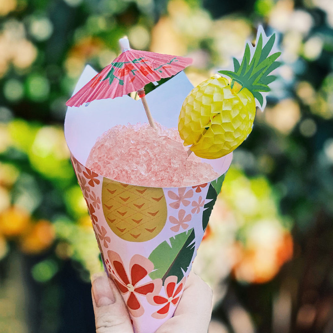 Snow cone with tropical pineapple pattern cone with umbrella against a blurred green background.