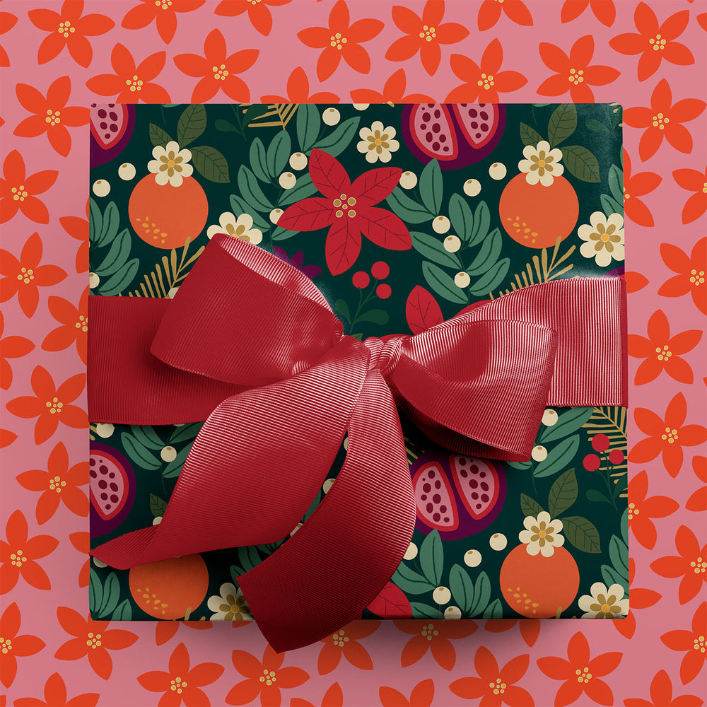 Gift wrapped in winter floral holiday wrapping paper with red ribbon, sitting on a coordinating background with a pink floral pattern.