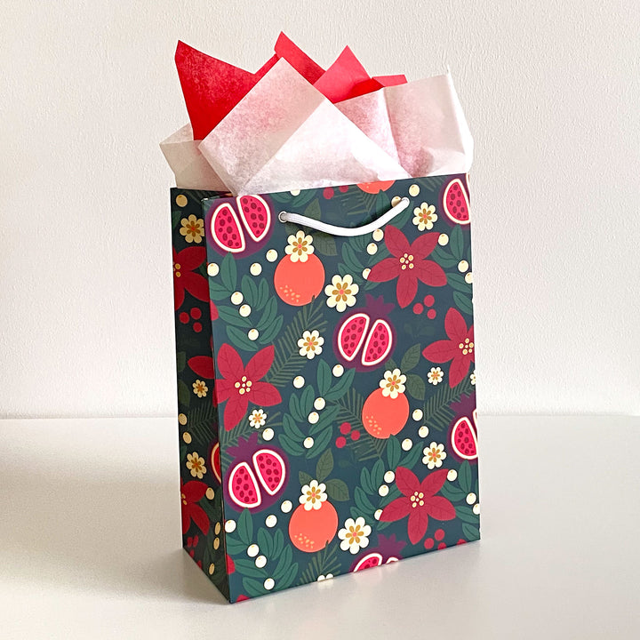 A gift bag featuring a holiday fruit and floral pattern with red and cream colored tissue paper
