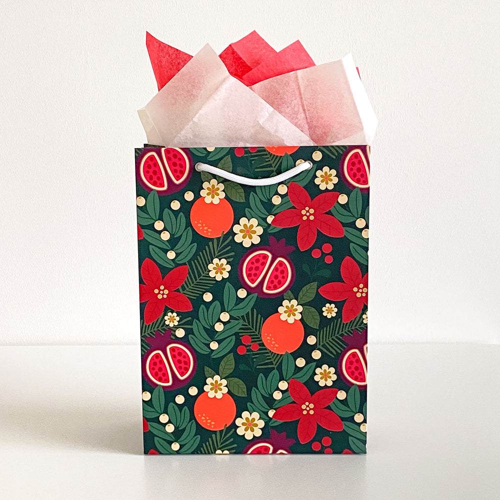 A gift bag featuring a holiday fruit and floral pattern with red and cream colored tissue paper