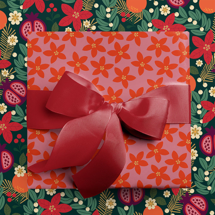 Gift wrapped in winter floral holiday wrapping paper with red ribbon, sitting on a coordinating background with a dark green floral & fruit pattern.