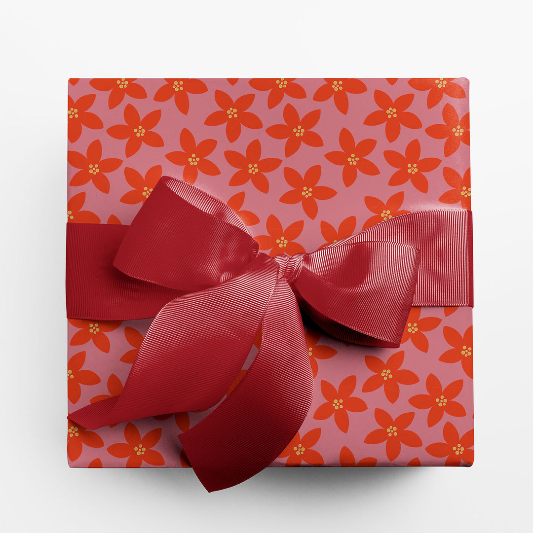 Gift wrapped with red and pink holiday floral wrapping paper and a large red bow on a white background.